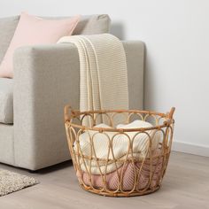 a wicker basket sitting on the floor next to a couch with blankets in it