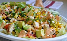 a white plate topped with a salad covered in avocado, corn and dressing