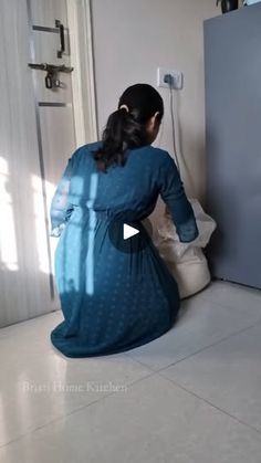 a woman sitting on the floor in front of a refrigerator with her back to the camera