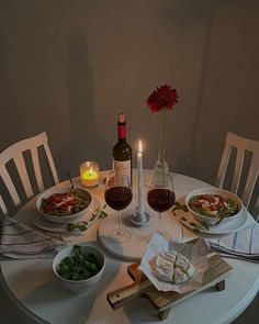 a white table topped with plates and bowls filled with food next to a bottle of wine