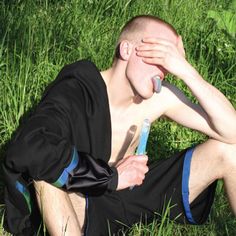 a man sitting in the grass with his hands on his face and holding a toothbrush to his nose