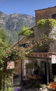 the outside of a building with flowers growing on it's roof and mountains in the background