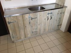 a kitchen with a metal sink and wooden cabinet doors on the wall, in front of a tiled floor