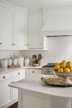 a bowl full of lemons sitting on top of a white countertop in a kitchen