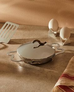 an empty pan sitting on top of a counter next to eggs and spatulas