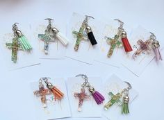 six different colored cross keychains on white paper with tiny charms attached to them