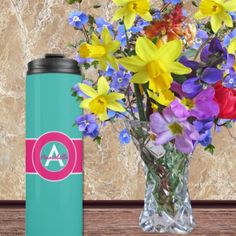 a vase filled with colorful flowers next to a blue travel mug on top of a wooden table