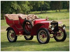 an old fashioned red car parked in the grass