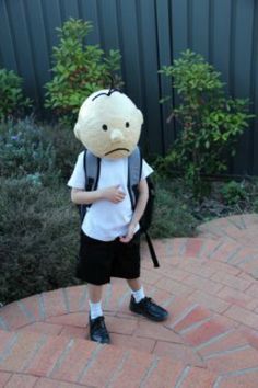 a young boy wearing a backpack with a stuffed animal on it's back standing in front of some bushes