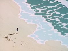 a man standing on top of a sandy beach next to the ocean with waves coming in