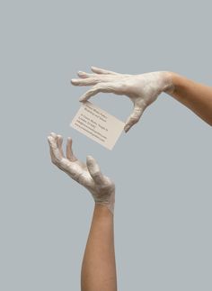 two hands with white powder on them reaching towards each other to catch a business card