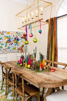 a dining room table decorated with christmas decorations and ornaments hanging from the chandelier