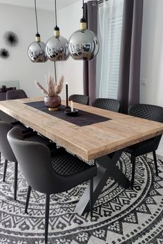 a dining room table and chairs in front of a window with hanging lights above it