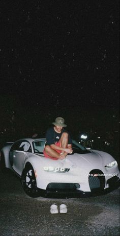 a woman sitting on top of a white sports car at night with her feet in the air