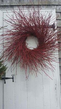 a red wreath hanging on the side of a white door next to a potted plant