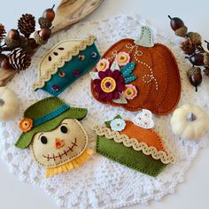 three felt pumpkins and two little scarecrows on a doily with pine cones