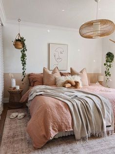 a bed with pink sheets and pillows in a bedroom next to hanging plants on the wall