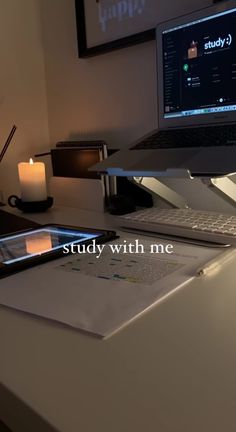 an open laptop computer sitting on top of a white desk next to a lit candle