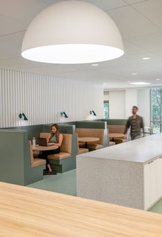 two people are sitting at desks in an office setting with open cubicles on the walls