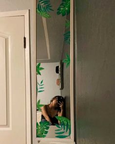 a man taking a selfie in a mirror with palm leaves on the wall behind him