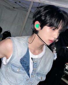 a young man with ear buds on his ears wearing a denim vest and white t - shirt