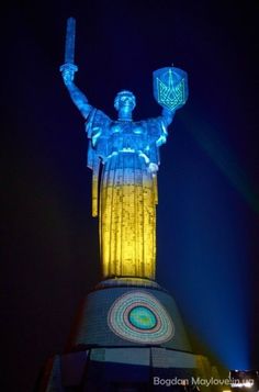 the statue of liberty is lit up in blue and yellow light at night with its arms raised