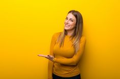 a beautiful young woman standing against a yellow wall pointing to the side with her hand