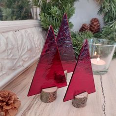 two red christmas trees sitting on top of a wooden table next to a candle holder