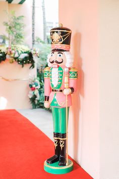 a wooden nutcracker standing on top of a red carpet next to a wall