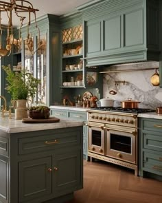 a kitchen with green cabinets and marble counter tops, an island in front of the stove