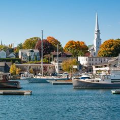 several boats are docked in the water near some houses and trees with fall foliage on them