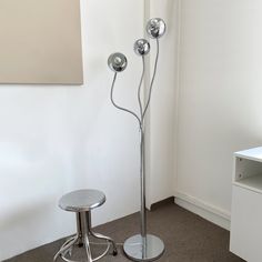 a metal floor lamp sitting next to a stool in a room with a painting on the wall