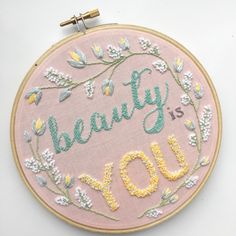 a pink embroidered wall hanging with the words beauty is you on it and some flowers