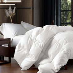 an unmade bed with white comforters and pillows on it in front of a window