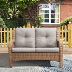 a wicker couch sitting on top of a rug next to a wooden fence and building