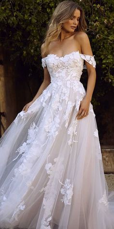 a woman in a white wedding dress with flowers on the skirt and off - shoulder