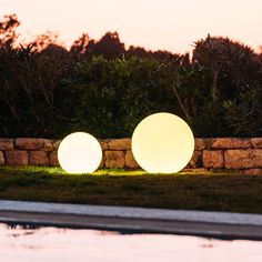 two large white balls sitting next to each other in the grass near a pool at sunset