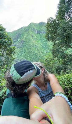 two people sitting on the back of a green chair in front of a lush green mountain