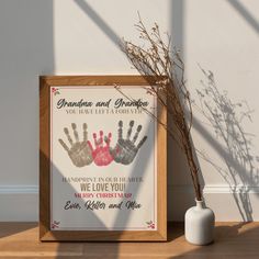 a wooden frame with two handprints on it next to a vase and plant