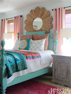 a bedroom decorated in turquoise and pink with a sunburst mirror above the bed