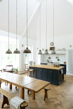 an open kitchen and dining room area with wooden table, benches, pendant lights hanging from the ceiling