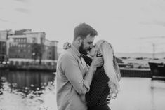 a man and woman kissing in front of a body of water with buildings behind them