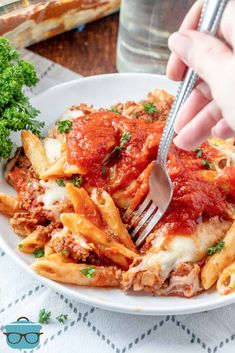 someone is eating some pasta with sauce and parmesan cheese on the side while holding a fork in their hand