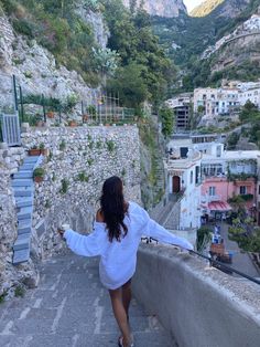 a woman is walking down the stairs in front of some buildings and trees, with her arms outstretched