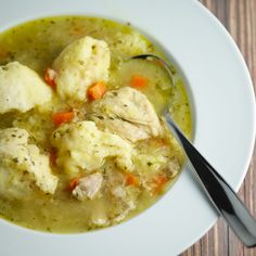 a white bowl filled with chicken and dumplings next to a spoon on top of a wooden table