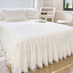 a white bed with ruffled bedspread and pillows