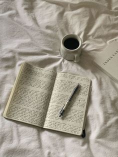 an open book, pen and coffee cup on a bed