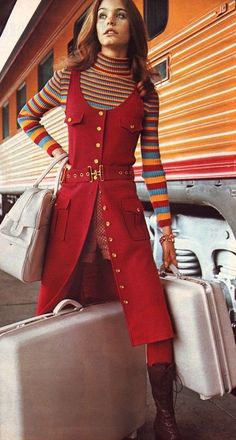 A beautiful young brunette woman wears a burgandy midi dress with gold buttons-the skirt is unbuttoned to show a pair of shorts underneath. She wears a 70s stripe T-shirt underneath. She holds white leather luggage. Susan Dey, Sassy Style, Partridge Family