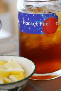 a bowl of fruit next to a jar of rocket fuel on a stove top with ice and water in it