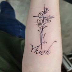 a cross and flowers tattoo on the left arm with words written below it in cursive font